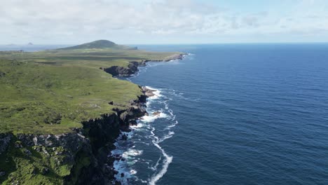 Valentia-island-coastline-with-lush-greenery-and-breaking-waves,-aerial-view