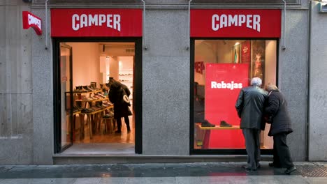 La-Gente-Mira-Escaparates-En-La-Multinacional-Española-De-Fabricación-Y-Venta-Al-Por-Menor-De-Calzado-Camper-Store-Mientras-Los-Peatones-Pasan-Por-El-Marco-En-Madrid,-España