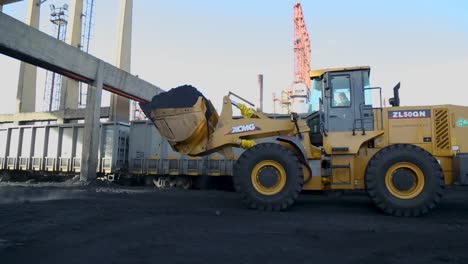 Gelber-Radlader-Transportiert-Kohle-Zu-Einem-Güterzug-Auf-Einem-Industriegelände,-Frühes-Morgenlicht