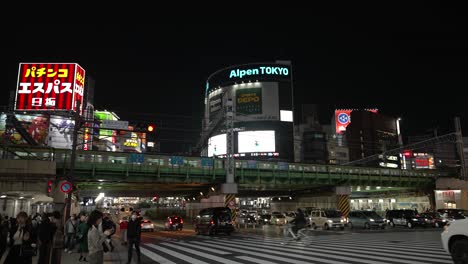 Tokyo's-Shinjuku-district-at-night-with-pedestrians-and-a-train-on-elevated-tracks