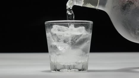 Primer-Plano-De-Una-Bebida-Que-Se-Vierte-Sobre-Cubitos-De-Hielo-En-Un-Vaso,-Contra-Un-Fondo-Oscuro