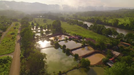 Fish-ponds-amidst-lush-greenery-in-oxapampa,-peru,-with-a-river-and-mountains-in-the-background,-at-sunrise,-aerial-view