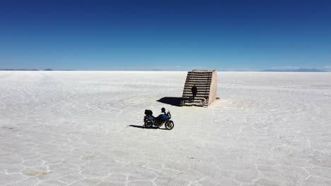 Man-leaves-motorcycle-on-salt-flat-lake-to-climb-salt-sculpture-stairs