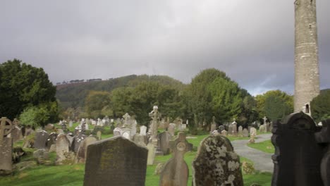 A-shot-panning-across-the-tombstones-at-Glendalough-graveyard-to-reveal-the-famous-Round-Tower-landmark-in-Wicklow,-Ireland