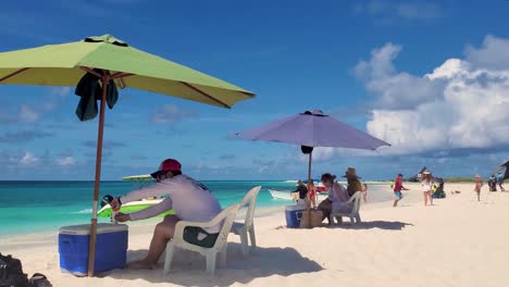 People-enjoy-sunny-day-at-Caribbean-beach,-putting-on-sunscreen-under-beach-umbrella