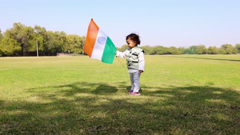 Kind-Läuft-Mit-Der-Indischen-Trikolore-Nationalflagge,-Die-Tagsüber-Auf-Einem-Grünen-Spielplatz-Weht