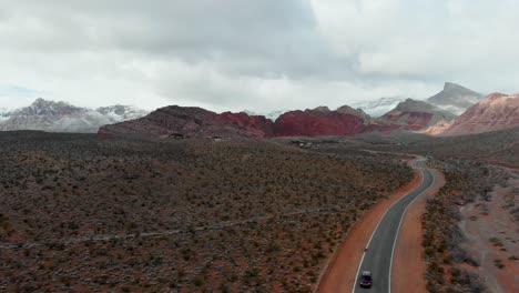 Aerial-drone-shot-along-a-small-road-with-snow-flurries-and-mountains-in-the-background