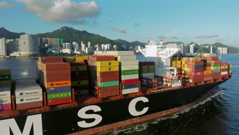 Drone-lifting-shot-revealing-tropical-urban-development-behind-large-container-vessel-on-a-bright-day