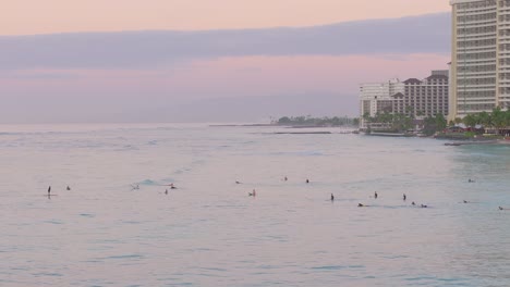 Tracking-Shot-of-Surfers-Swimming-out-to-Sea-at-Vacation-Resort,-Waikiki,-Dusk