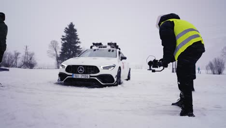 Coche-Atrapado-En-Una-Densa-Nieve-En-La-Pista-De-Carreras,-La-Gente-Alrededor-Mira-Y-Filma-En-Cámara