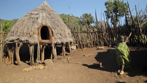 Toma-En-Cámara-Lenta-De-Niños-Africanos-Caminando-Junto-A-Una-Cabaña-De-Una-Aldea-Tribal-En-El-Este-De-Uganda