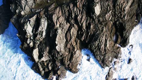 Luftaufnahme-über-Felsen-Und-Weiße-Wasserwellen,-Die-In-Zeitlupe-Entlang-Der-Küste-Von-Cornwall-Plätschern