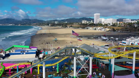 Vista-Aérea-Sobre-El-Estado-De-California-Y-La-Bandera-Estadounidense-En-La-Cima-Del-Muelle-De-Santa-Mónica-En-La-Soleada-La