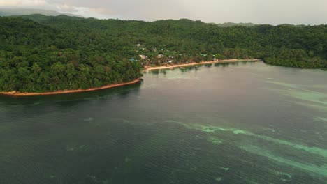 Idyllic-view-of-transparent-ocean-waters-along-tropical-island-coastline-with-quaint-fisherman-village-and-lush-jungles