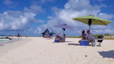 pan-right-people-enjoy-summer-caribbean-beach,-man-put-sunscreen-on-his-girlfriend