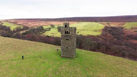 Old-derelict-castle,-monument,-disused-stone-tower,-with-people-walking-around-and-flying-a-drone