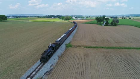 An-Aerial-View-of-an-Approaching-Steam-Passenger-Train,-Blowing-Smoke-and-Steam,-in-Slow-Motion,-on-a-Partially-Sunny-Day