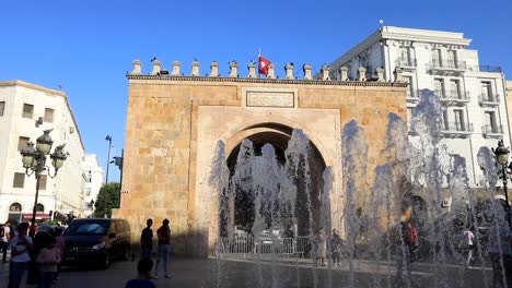 Sunlit-view-of-the-historic-Tunis-city-gate-with-fountain-in-the-foreground,-vibrant-urban-life