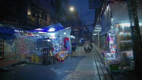 Roller-Fährt-Durch-Chaotische-Dunkle-Straße-Mit-Geschäften-In-Bangkok