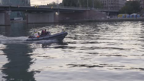 Bote-Inflable-Con-Tripulación-En-El-Río-En-Frankfurt-Al-Atardecer,-Paisaje-Urbano-Y-Puente-En-Segundo-Plano.