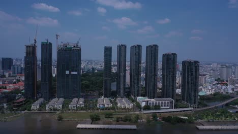 Ho-Chi-Minh-City,-Saigon-River-and-Binh-Thanh-skyline-on-sunny,-clear-day-flying-in-towards-new-buildings-on-the-site-of-former-Ba-Son-shipyard-from-drone