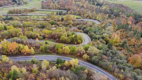 Autumn-foliage-woods-landscape-with-curvy-serpentine-road,-aerial-panorama