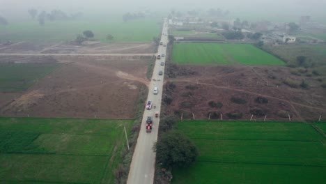 Luftaufnahme-Einer-Viel-Befahrenen-Landstraße-In-Alipur,-Pakistan,-Die-Grüne-Felder-Trennt,-Mit-Verkehr-Und-Dunst