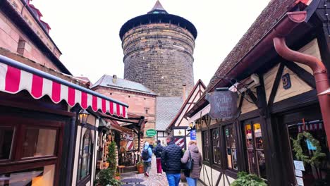 Tourists-browsing-hand-made-gifts-at-the-Handwerkerhof-in-Nuremberg,-Germany-with-a-view-of-the-charming-street-and-castle-tower