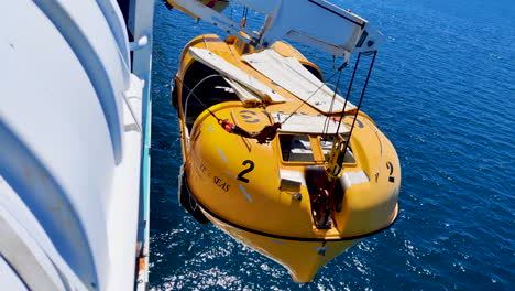 In-readiness-for-safety,-cruise-ship's-lifeboat-dangles-from-cranes,-poised-to-swiftly-deploy-into-the-water,-ensuring-preparedness-and-passenger-security-amid-the-vast-expanse-of-the-open-sea