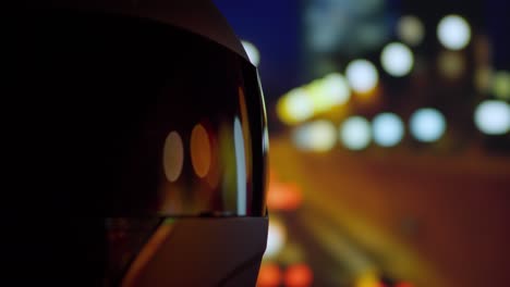 City-lights-and-night-traffic-reflected-on-a-focused-motorcycle-helmet