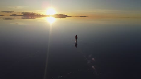 Mujer-Camina-Sobre-La-Superficie-Reflectante-Del-Lago,-Salar-De-Uyuni-Puesta-De-Sol-Bolivia