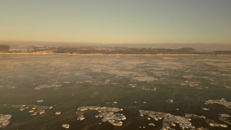 Drone-view-going-towards-the-coast-of-the-Orleans-Island,-Quebec,-Canada,-from-the-St-Lawrence-river-Seaway,-on-a-very-cold-Winter-morning