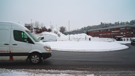 Several-different-cars-going-around-a-snow-covered-roundabout-on-an-overcast-winter-day