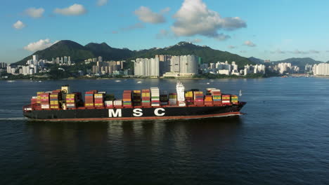 Container-ship-in-front-of-urban-high-rise-development-on-mountainous-island