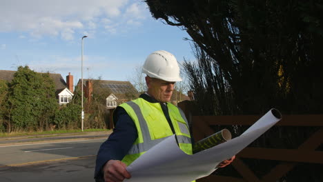 An-architect-structural-engineer-examining-plans-in-the-driveway-of-a-large-building-on-a-construction-site-in-a-residential-street-with-traffic-on-the-road-in-the-background