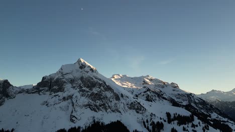 Fronalpstock-Switzerland-Glarus-Swiss-alps-low-sun-on-peaks-with-moon-high-above-blue-sky