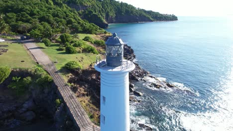 Drone-Volando-Alrededor-De-La-Parte-Superior-Del-Faro-En-Vieux-fort-Con-Costa-Irregular-En-El-Fondo,-Guadalupe