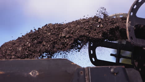 Slow-motion-footage-of-ground-up-road-asphalt-being-churned-out-of-a-machine-and-into-the-back-of-a-construction-truck