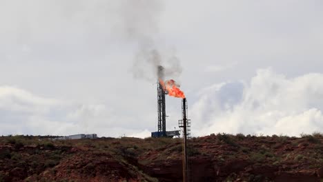 Industrial-oil-rig-flaming-gas-in-a-desert-setting-under-a-cloudy-sky,-environmental-impact