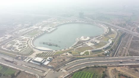 Carretera-Con-Vista-De-Drones-Del-Lago-Rajkot-Atal-Y-Muchos-Vehículos-Diferentes-Circulan-Por-La-Carretera-Y-Se-Ven-Grandes-Lagos,-Nuevo-Hipódromo-De-Rajkot,-Atal-Sarovar