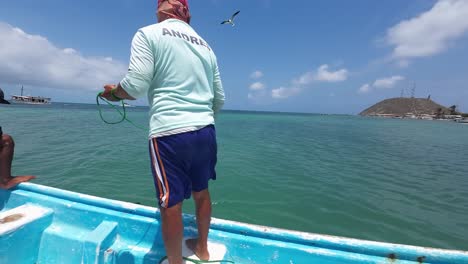 Pescador-Lanzando-Red-Desde-Un-Barco-En-Un-Día-Soleado,-Con-Agua-Azul-Clara-Y-Un-Barco-En-La-Distancia,-Toma-De-Acción-Dinámica