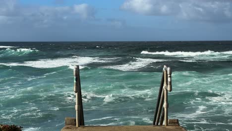 Stairs-leading-down-to-ocean-on-a-beautiful-day-with-waves-and-blue-green-water