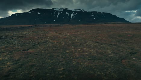 Toma-Aérea-De-Un-Dron-Que-Roza-El-Terreno-Rocoso-Y-Se-Inclina-Hacia-Arriba-Para-Revelar-Una-Hermosa-Cadena-Montañosa-Cubierta-De-Nieve.