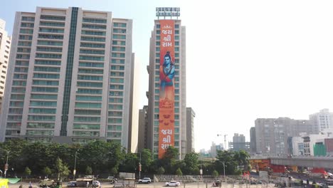 Vista-Aérea-De-Drones-De-Rajkot-Donde-La-Pancarta-De-Modhu-Jayate-Ram-Es-Visible-En-El-Gran-Edificio-Plateado-Y-Muchos-Vehículos-Circulan-Por-La-Carretera