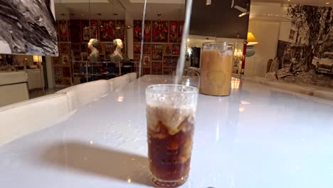 Slow-motion-pour-milk-into-ice-coffee-and-spilling-it-on-white-laminate-table