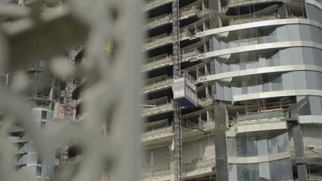 Die-Beobachtung-Eines-Im-Bau-Befindlichen-Wolkenkratzers-In-Dubai,-Vereinigte-Arabische-Emirate,-Zeigt-Einen-Kran,-Der-Arbeiter-Auf-Die-Spitze-Des-Hoch-Aufragenden-Bauwerks-Hebt,-Das-Nach-Seiner-Fertigstellung-Normalerweise-Eine-Höhe-Von-180-Metern-Erreicht