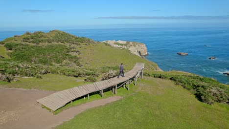 Bird's-eye-view-of-a-young-man-walking-up-the-pier-of-souls-in-Cucao-in-Chiloe-Chile,-alone-meditating