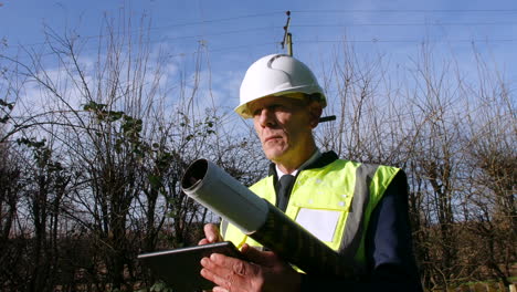 Low-angle-portrait-of-a-concentrating-architect-building-inspector-inspecting-a-construction-site-with-a-tablet-and-architectural-plans