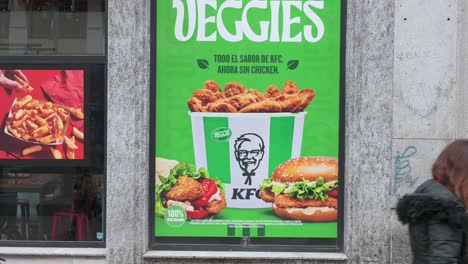 Fußgänger-Gehen-An-Einer-Straßenwerbung-Von-KFC-Vorbei,-Die-Ein-Neues-Vegetarisches-Gericht-Namens-Veggies-Vorstellt,-Das-In-Den-Fast-Food-Ketten-In-Spanien-Erhältlich-Ist