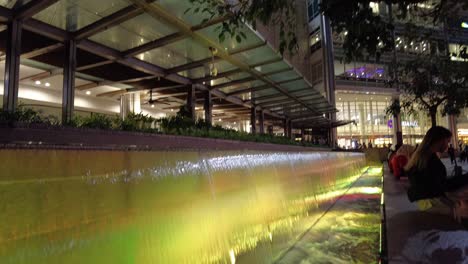 Nighttime-view-of-the-mini-waterfalls-in-front-of-the-mall-at-the-base-of-the-Petronas-Twin-Towers,-an-iconic-symbol-of-Malaysia's-prosperity-and-the-country's-booming-oil-based-economy